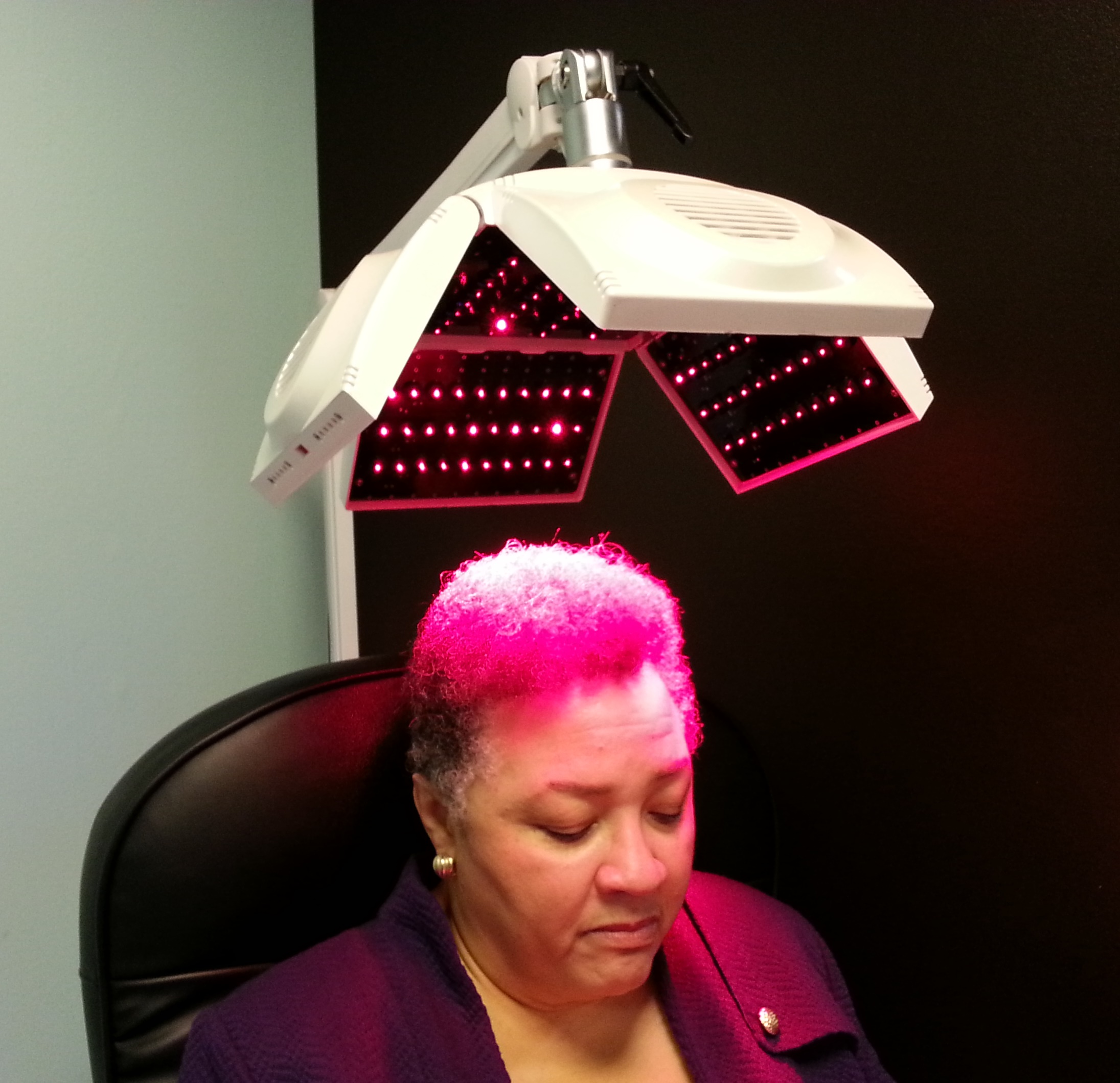Seated salon client beneath a red light hair treatment device